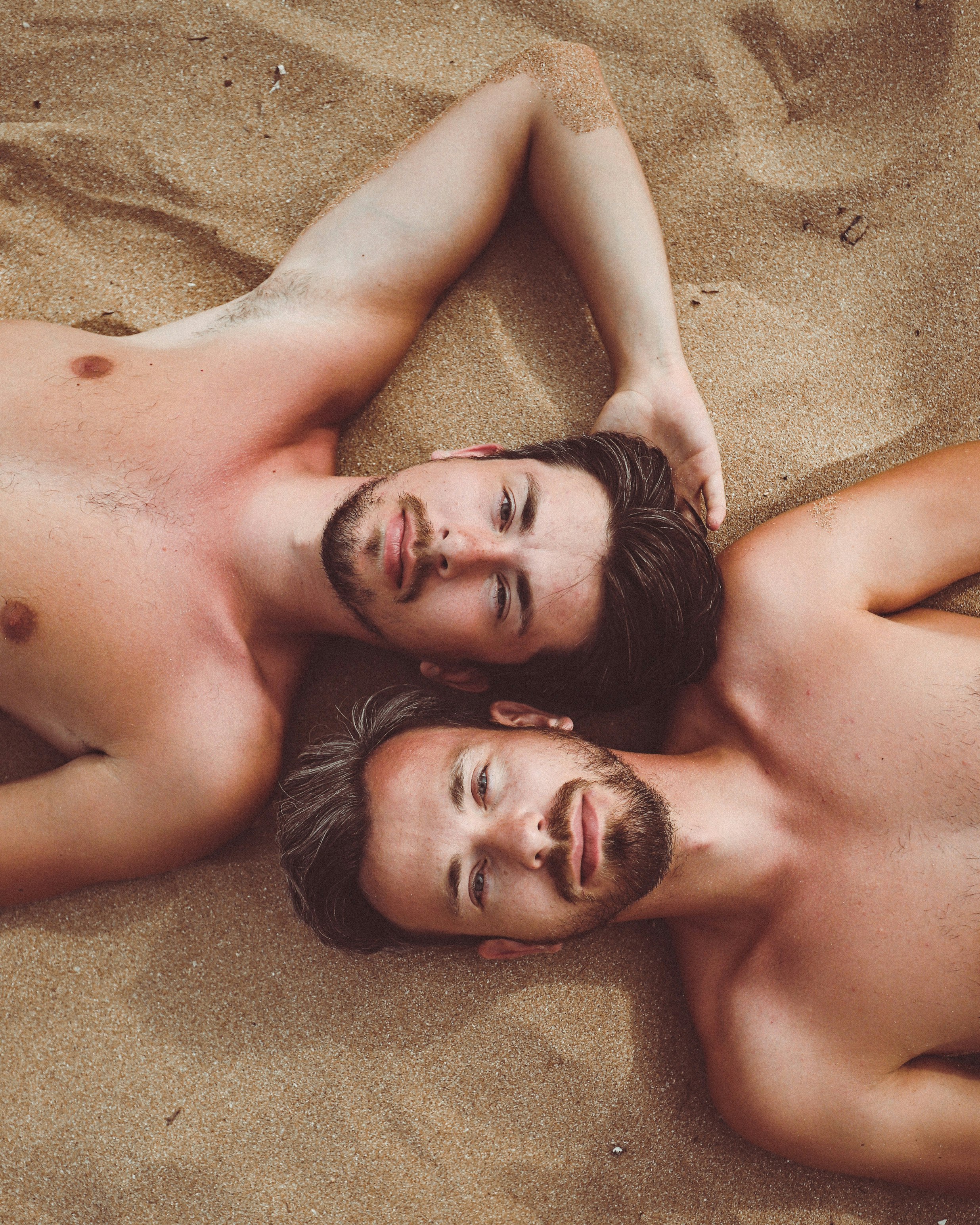 topless man lying on brown sand during daytime